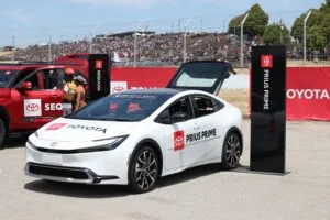 A Toyota Prius Prime on display at an outdoor car exhibition with spectators in the background.