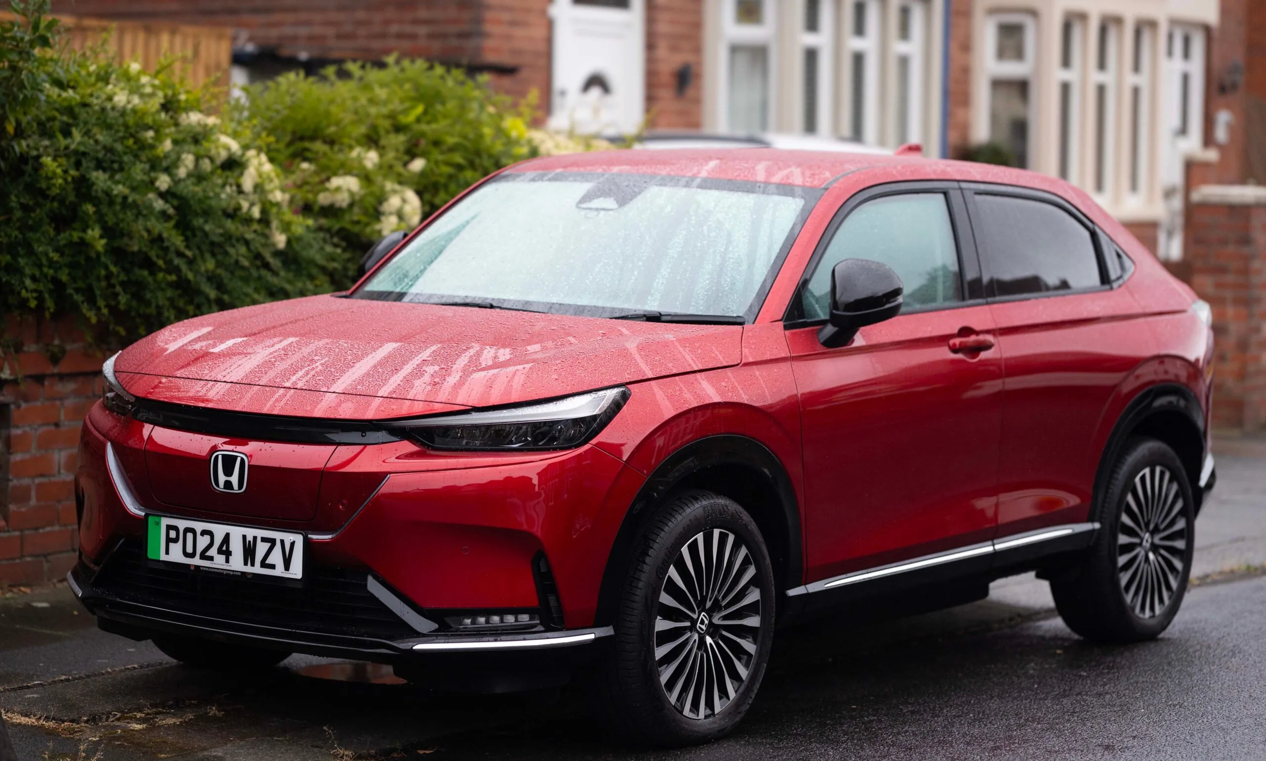 A vibrant red Honda SUV parked on a rainy suburban street, showcasing modern design.